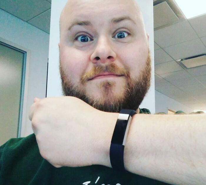 A man with a beard and wide eyes holds up his wrist to show a fitness tracker, a real photo that makes your brain question if it was edited.