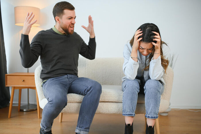 A man yelling at a crying woman on a couch, depicting a situation where red flags were ignored.