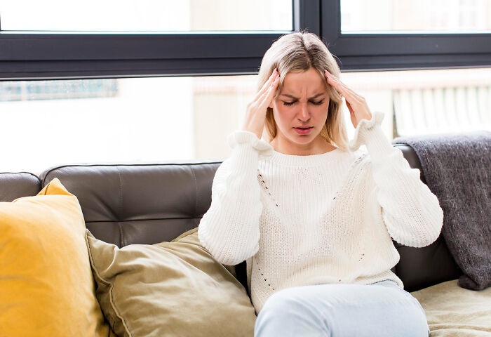 A blonde woman on a couch holding her head, illustrating the consequences of ignoring red flags.