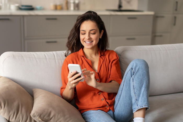 A smiling woman with great hair on a couch, looking at her phone, depicting someone who ignored red flags.