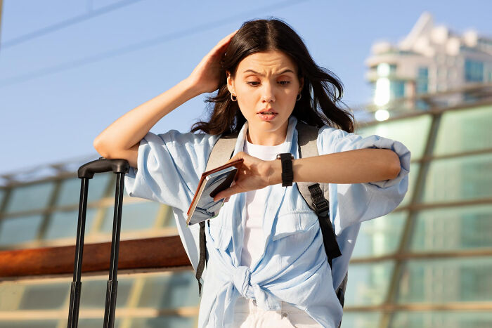 Young woman with luggage looking at her watch in shock. Ignoring red flags because the person was hot.