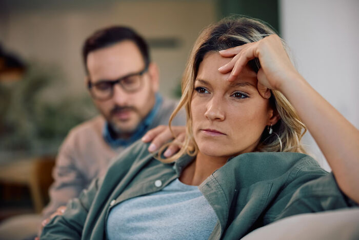 A woman looks distressed while a man touches her shoulder, highlighting ignored red flags.