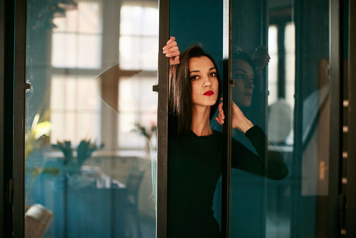 A woman with great hair and red lipstick looking through a glass door, representing ignoring red flags.