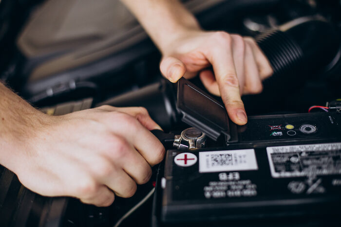 Hands working on a car battery, depicting one of the unpopular industries that actually make millions.