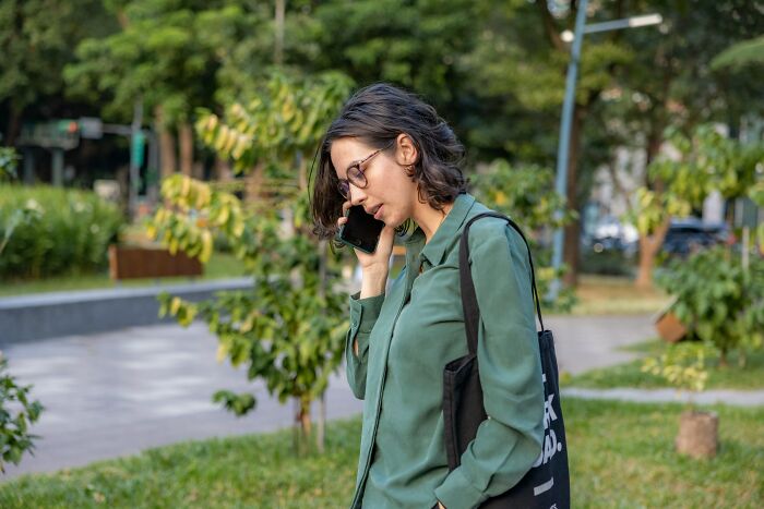 A woman in a green shirt and glasses talking on a smartphone outdoors, depicting a moment of instant justice.