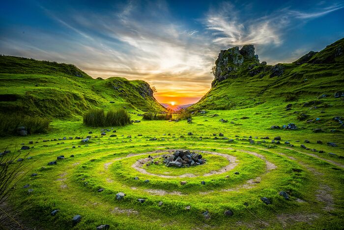 A serene landscape with a sunset over green hills and a circular stone arrangement, contrasting with mansplaining examples.