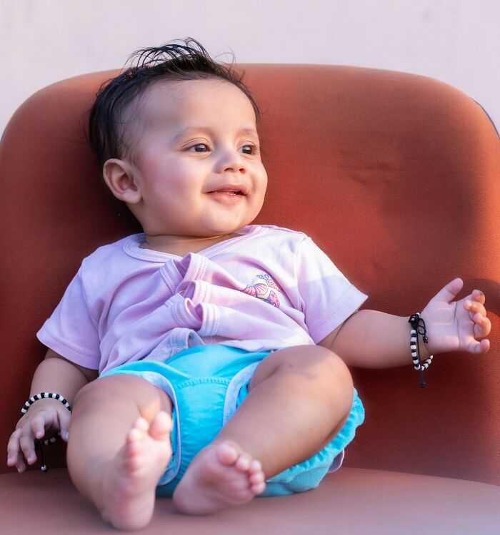 A smiling baby in a pink shirt and blue shorts sits on an orange chair. Products, Trends, and Items.