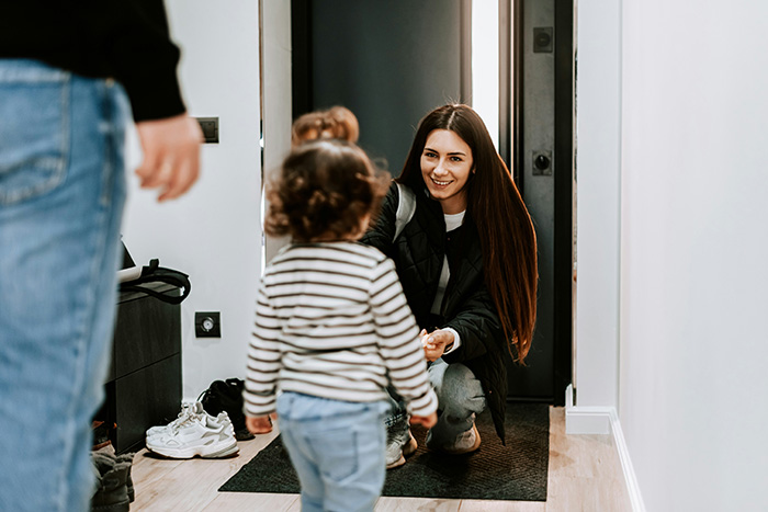 A nanny happily greeting a child at the doorway, showing the dynamic of a nanny and family.