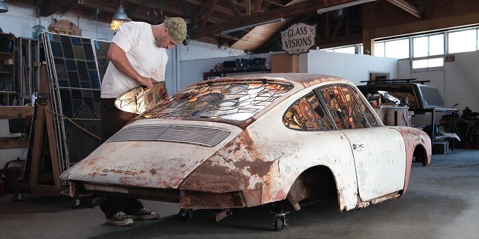 Artist working on the stained-glass sculpture of a burned and rusted Porsche 911.