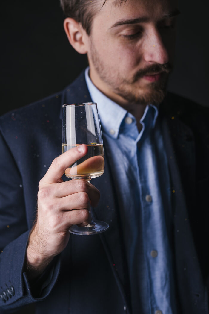 A man in a suit holding a glass of champagne, regretting his spending at a wedding.