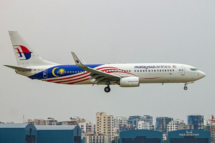 A Malaysia Airlines plane in flight over a city skyline, representing one of the greatest unsolved mysteries in aviation.