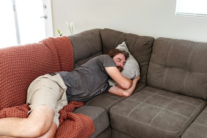 A man sleeping on a brown couch with a pillow, feeling smarter with curious facts.