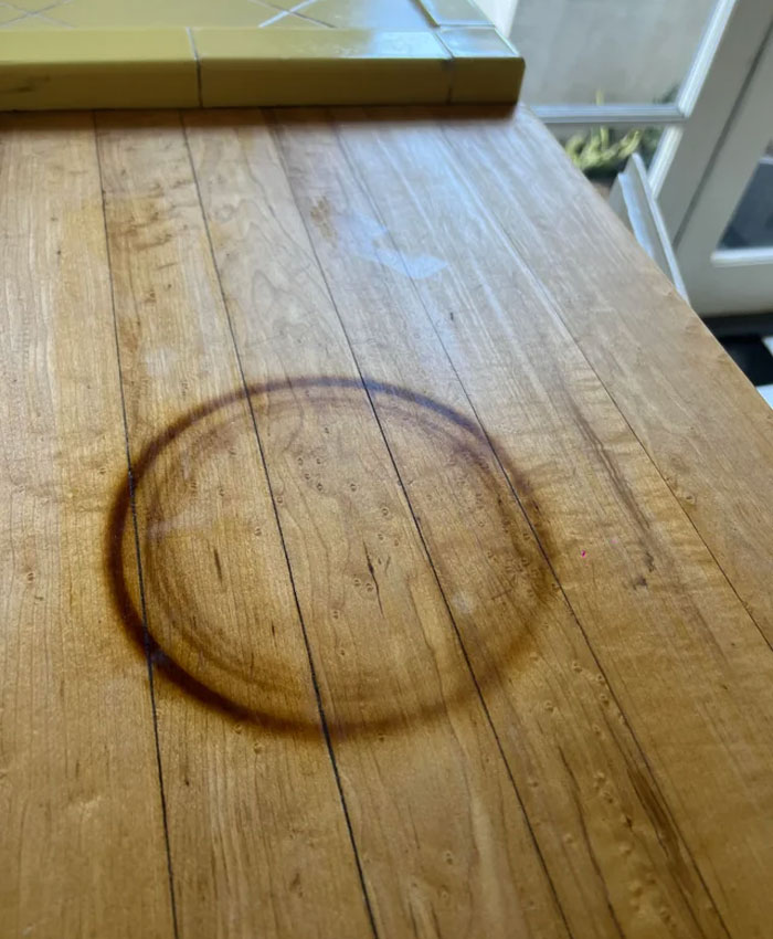 People ask others for help fixing a dark, circular stain on a light wooden table.