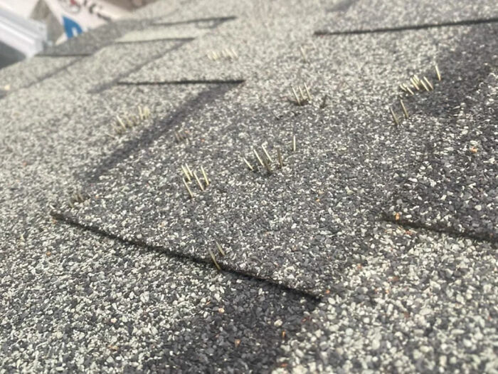 Close-up of a damaged shingle roof with many exposed nails sticking out, showing problems to be fixed.