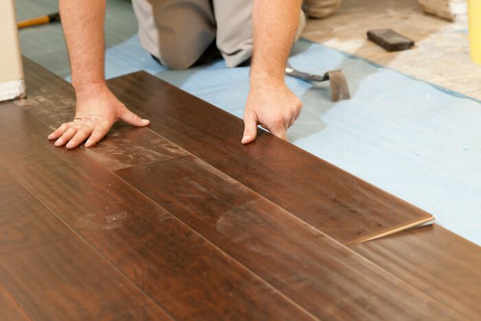 Worker installing laminate flooring, illustrating industries where people are getting scammed through shoddy work.