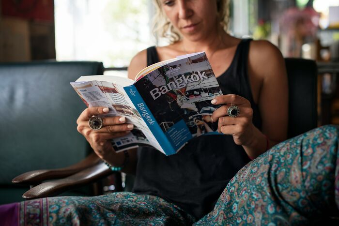 A woman reads a travel guide about Bangkok, unaware of how people are getting scammed in various industries.
