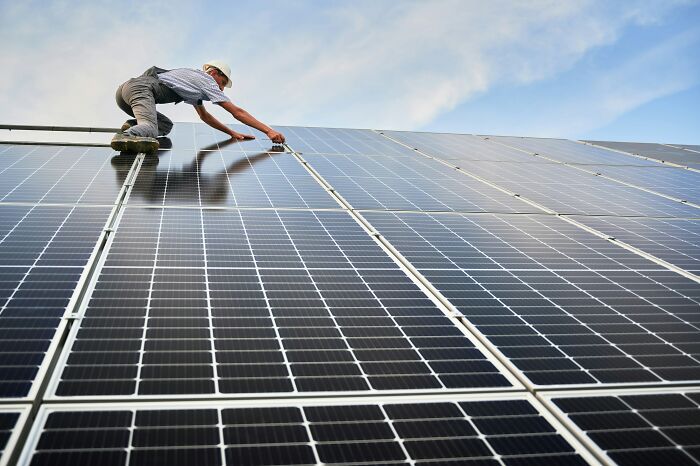 A worker on a roof installing solar panels, subtly suggesting how people are getting scammed.