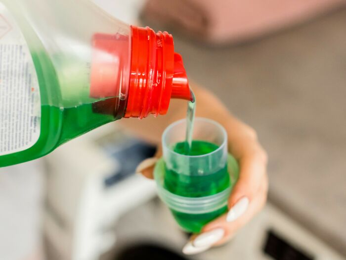 Hand pouring laundry detergent into a cap, representing everyday products where people are getting scammed with hidden costs.
