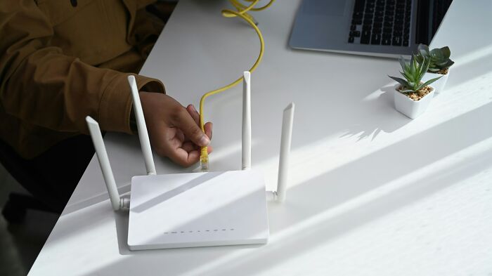 A person connects an ethernet cable to a router, illustrating how people are getting scammed with tech services.