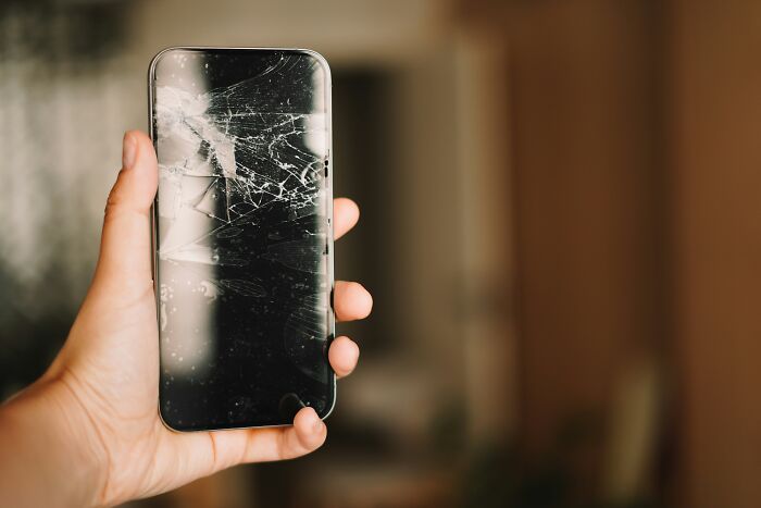 A hand holding a smartphone with a cracked screen, illustrating the hidden scams people fall into.