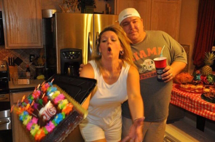 Hilarious photo of a woman moments before dropping a birthday cake with lit candles, looking surprised.