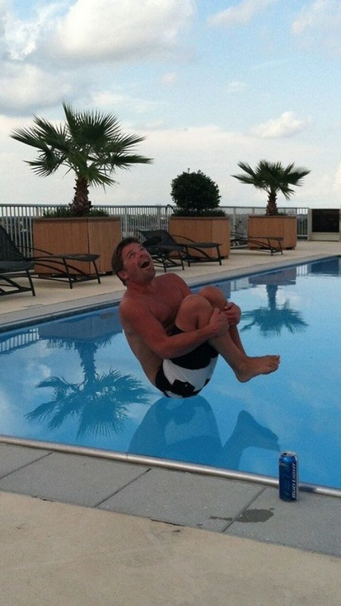 A man in hilarious photos mid-air above a pool, legs tucked, moments before disaster, with palm trees in background.