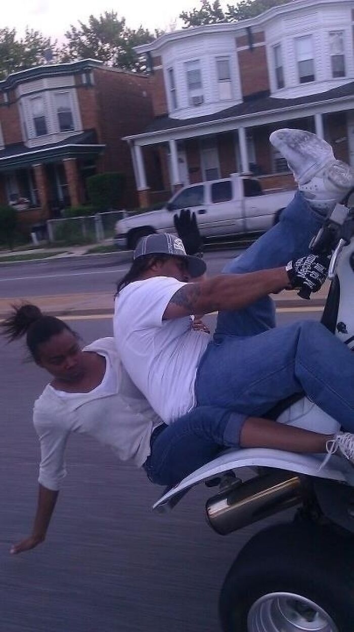 A woman about to fall off the back of a motorcycle, captured moments before disaster struck.