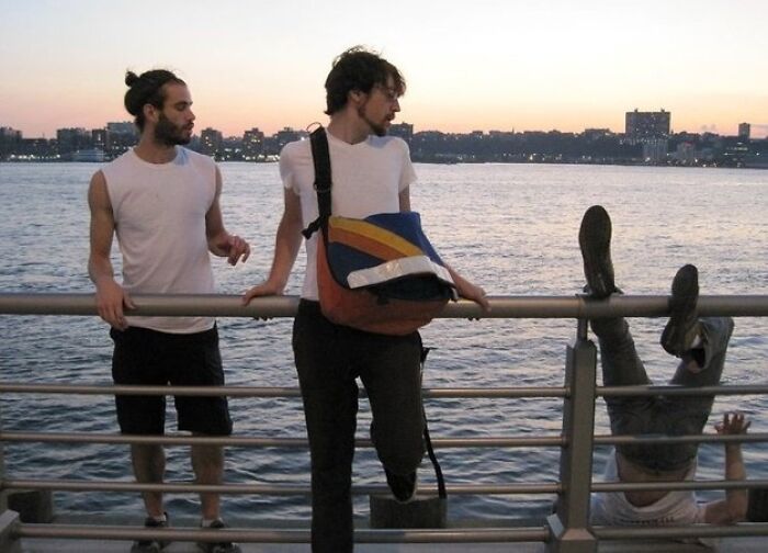 Hilarious photo of two men by a railing, as a third person falls backward into the water, moments before disaster.