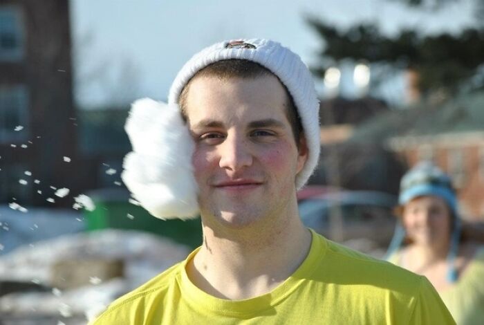 Hilarious photo of a man hit by a snowball, a white puff on his face, taken moments before disaster.