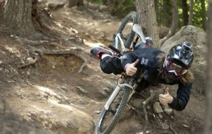 Hilarious photo of a mountain biker giving a thumbs up while falling sideways with their bike, moments before disaster.