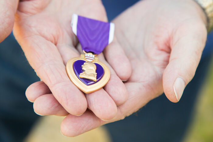 Hands gently holding a Purple Heart medal, honoring World War II veterans and their extraordinary stories.