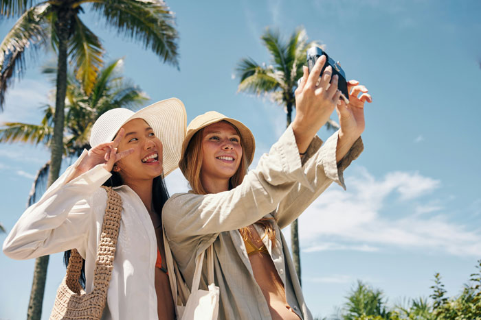 Travel influencer taking a selfie with a friend, both wearing hats, depicting a solo trip lie. Travel influencer taking a selfie with a friend, both wearing hats, depicting a solo trip lie.