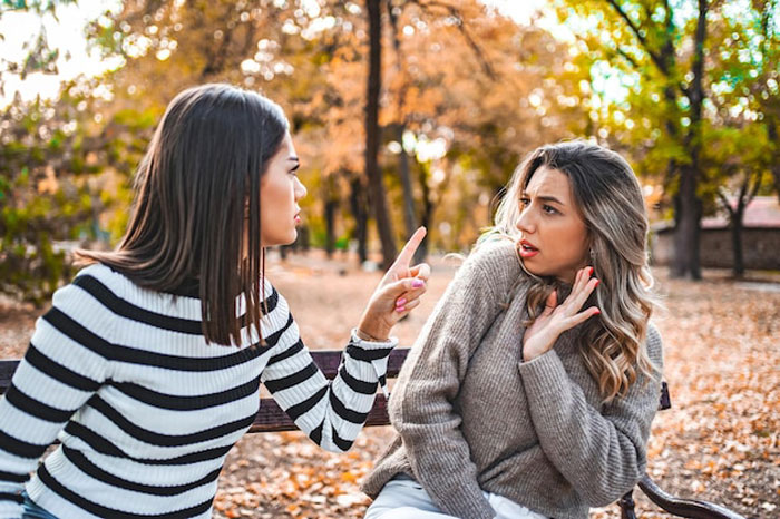 Two women arguing in a park, representing a friend calling out a travel influencer for lying about solo trips. Two women arguing in a park, representing a friend calling out a travel influencer for lying about solo trips.