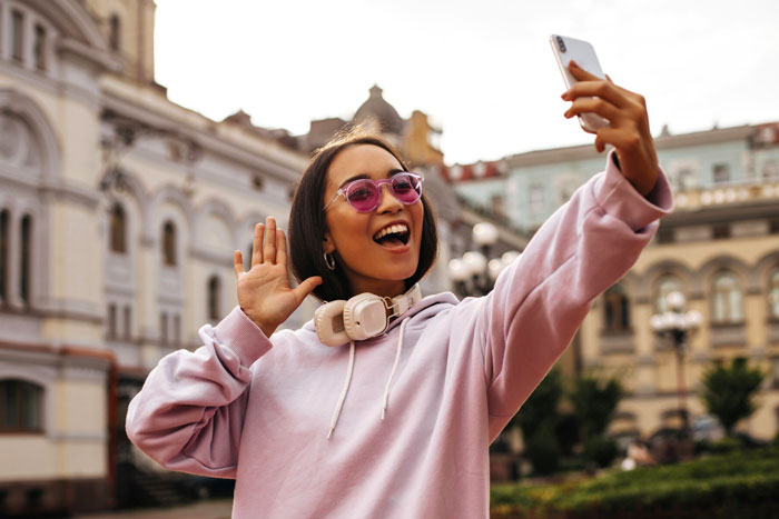A smiling travel influencer with sunglasses takes a selfie in a city, possibly lying about solo trips and budget. A smiling travel influencer with sunglasses takes a selfie in a city, possibly lying about solo trips and budget.