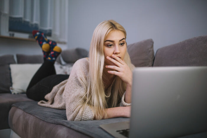 A woman lying on a couch, looking intently at a laptop screen, illustrating the experience of psycho moments from partners.