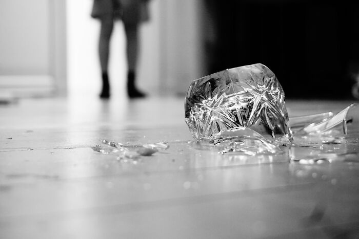 A broken glass on the floor with a person in the background, showing psycho moments.