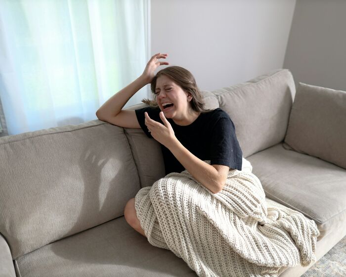 A distressed woman cries on a couch, covered with a blanket, reacting to a psycho moment from a partner, saying 'never again'.