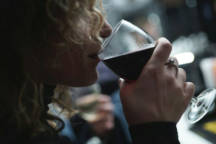 A woman with curly hair sips red wine, showcasing a ring on her finger, reflecting on psycho moments with partners.