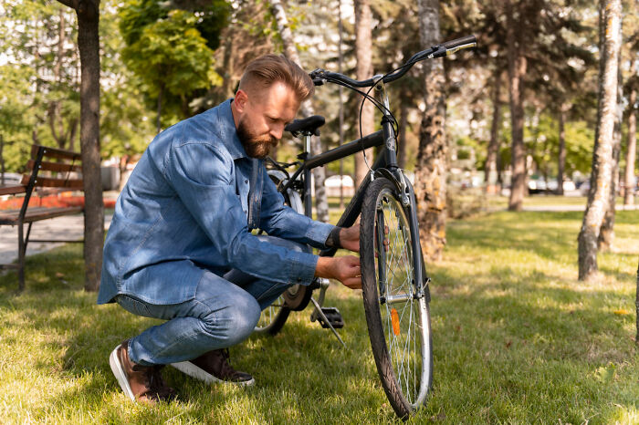 A man fixing a bicycle in a park, illustrating a moment of calm amidst partner issues.