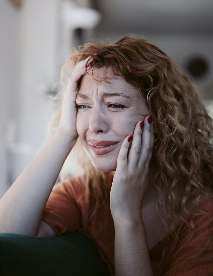 A crying woman with red hair holding her head, experiencing psycho moments from partners.