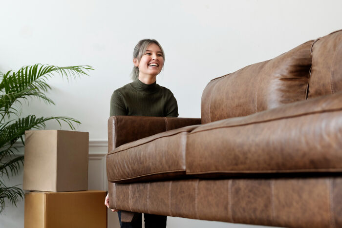 A smiling woman moving a large brown couch, illustrating psycho moments from partners.