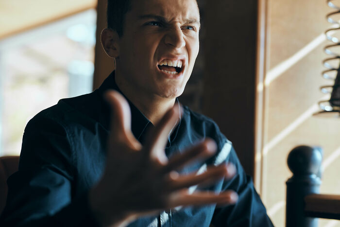A man with a pained expression and open hand gestures expresses his frustration, reliving psycho moments from partners.