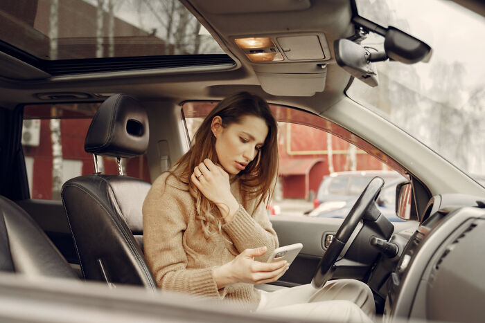 A woman looking distressed while sitting in her car and holding her phone, depicting psycho moments from partners.