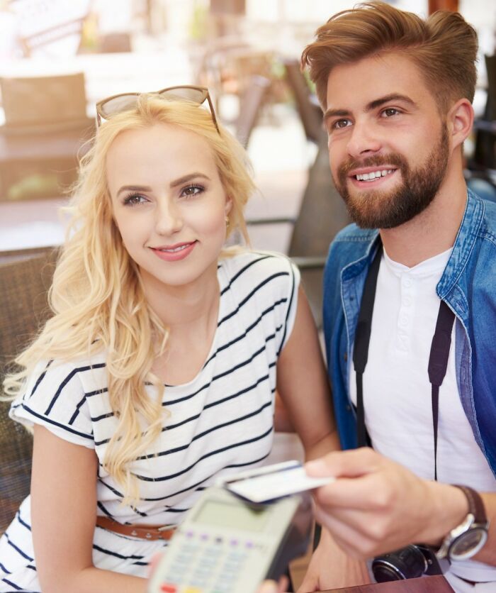 A happy couple paying with a card at an outdoor cafe, illustrating psycho moments from partners.