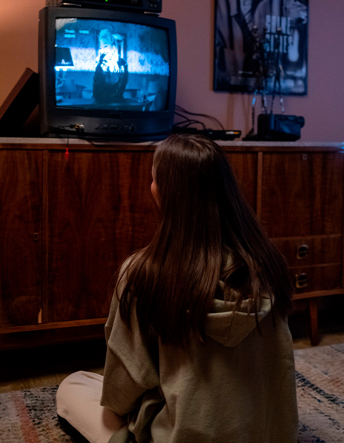 A young woman watches an old television, considering how sibling disputes can lead to tragedy.
