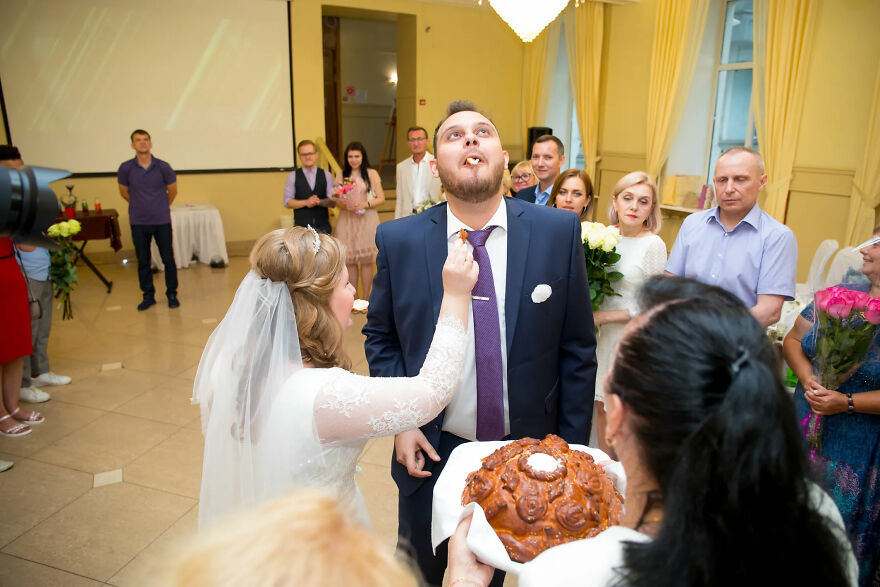 A funny wedding photo of a bride feeding the groom in front of guests.