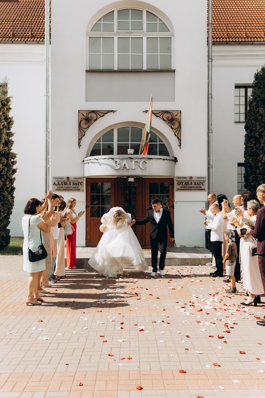 Funny wedding photo of a bride running while being held by the groom as guests clap during their exit.