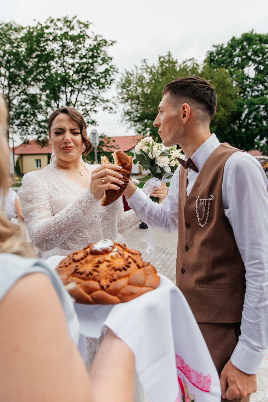 A bride and groom making funny faces while breaking bread at their wedding.