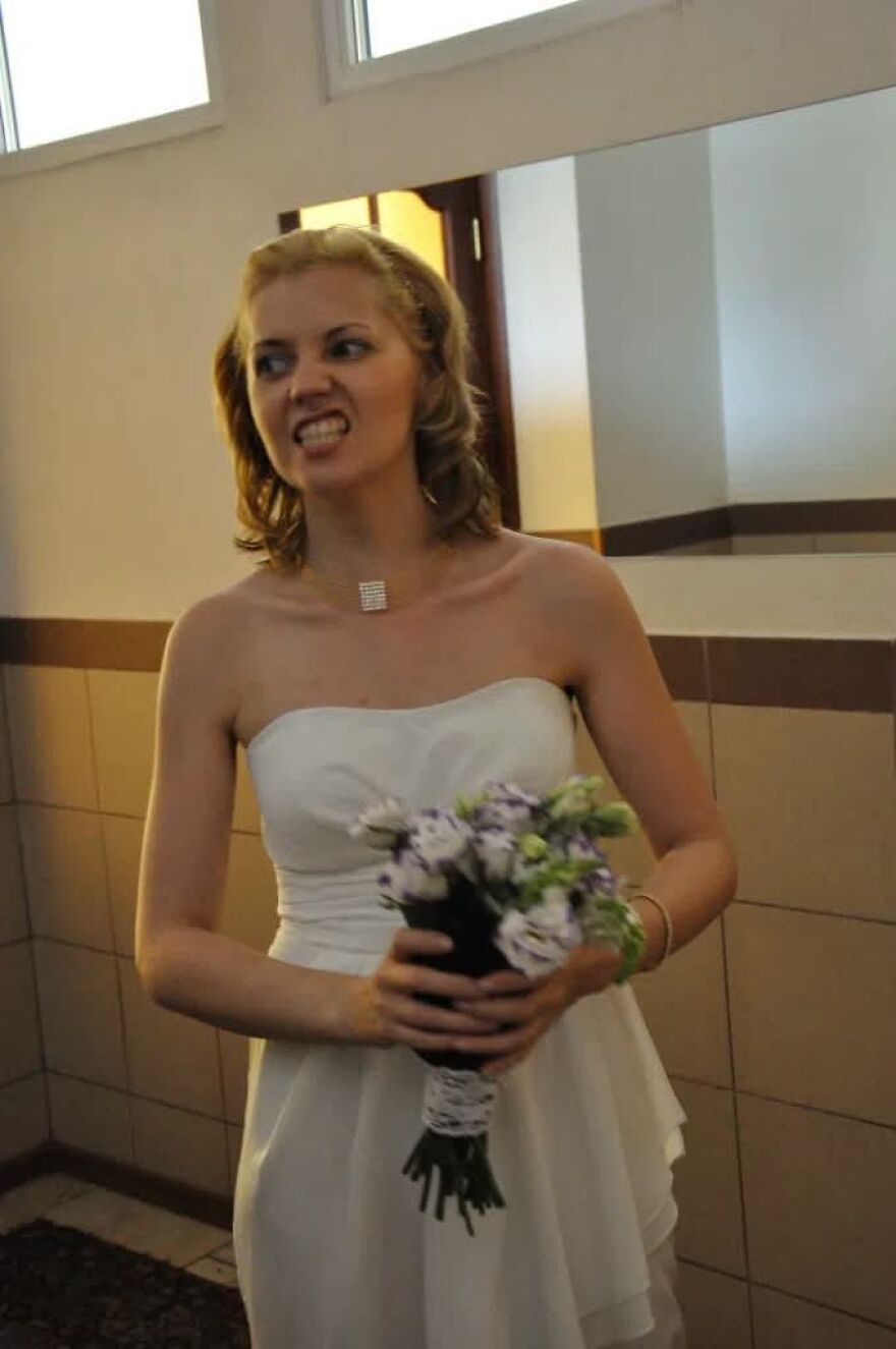 A bride making a funny cringe face while holding a bouquet at her wedding.