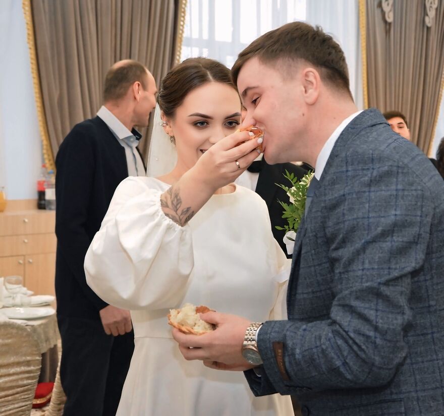 A bride feeding her groom a piece of bread, a funny wedding photo capturing a silly moment.